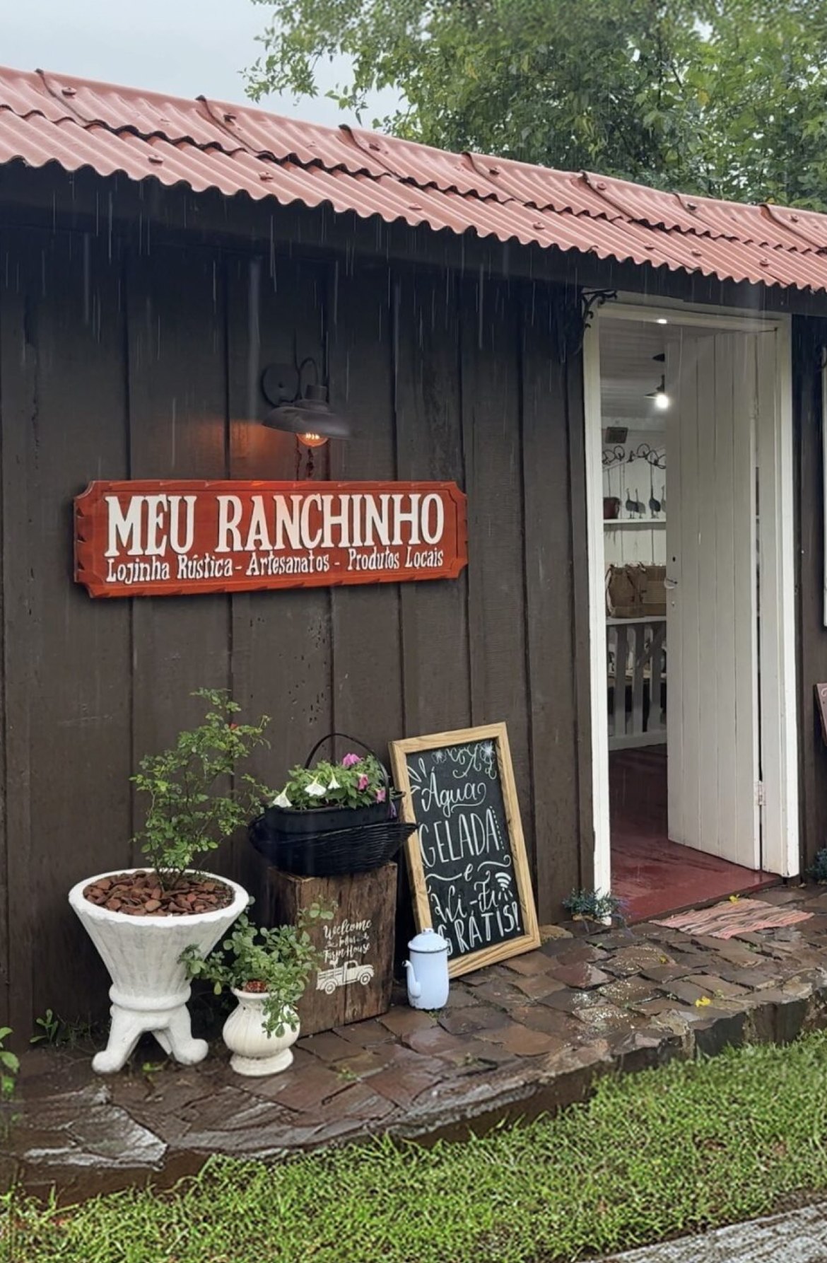 Fachada da lojinha Meu Ranchinho, com vasos de plantas e lousa na entrada